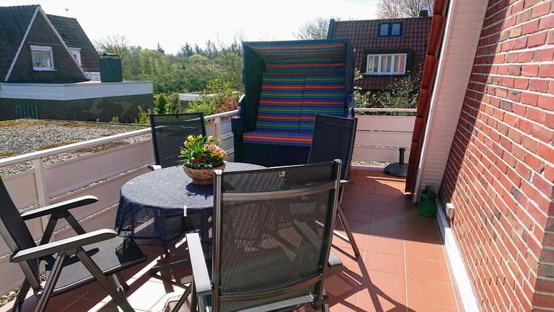 Sonnenterrasse des Haus MaJoMi mit bunt gestreiftem XXL-Strandkorb, Tisch, Gartenstühlen und Blumenschale